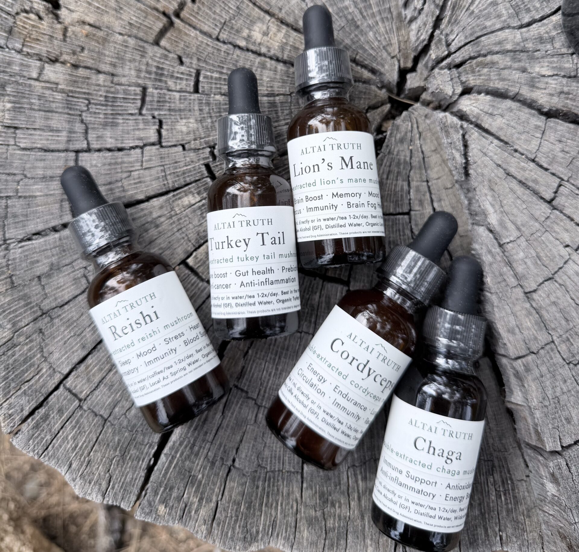 Altai Truth mushroom tinctures on natural wood surface — Lion’s Mane, Reishi, Chaga, Cordyceps, Turkey Tail wellness extracts.